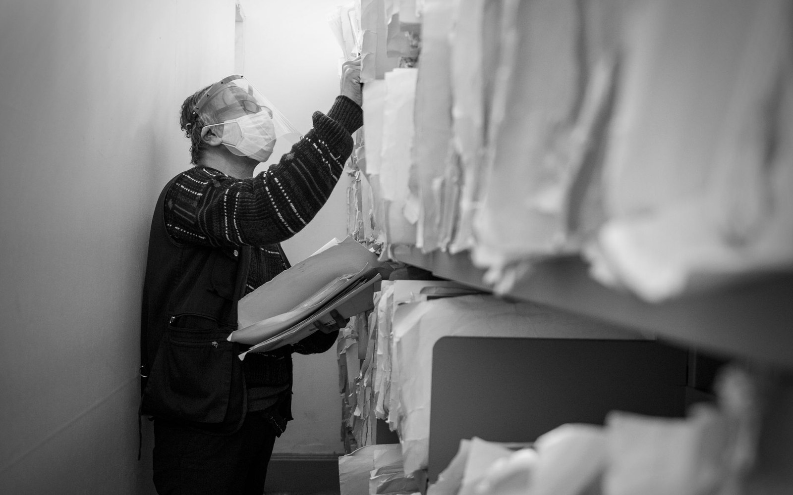 An open archive box with a typed finding aid and manila folders, hands of an adult archivist visible lifting one folder