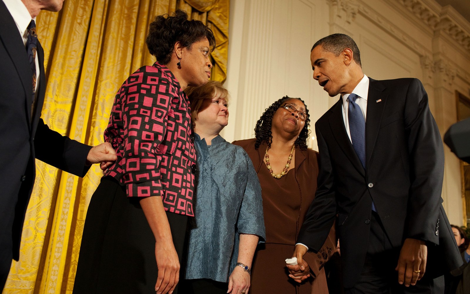 President Obama speaks closely with a group of women in an ornate gold-curtained room