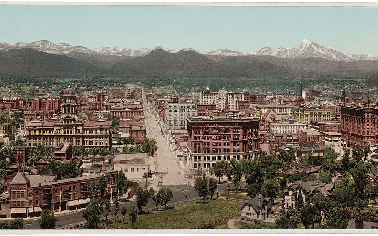 Historic aerial view of a city grid with brick buildings and snow-capped mountains beyond