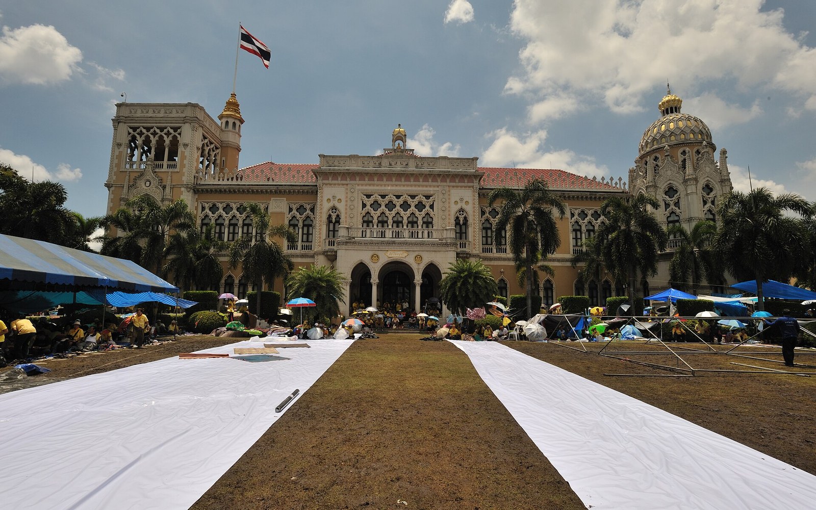 Government House in Bangkok with domed towers, flag flying, and tents camped on the lawn